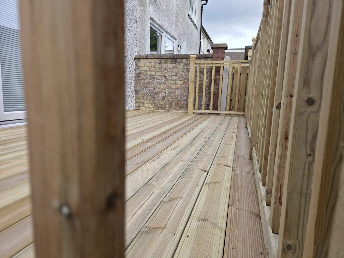 Grooved deck boards running past a spindle balustrade towards a house wall