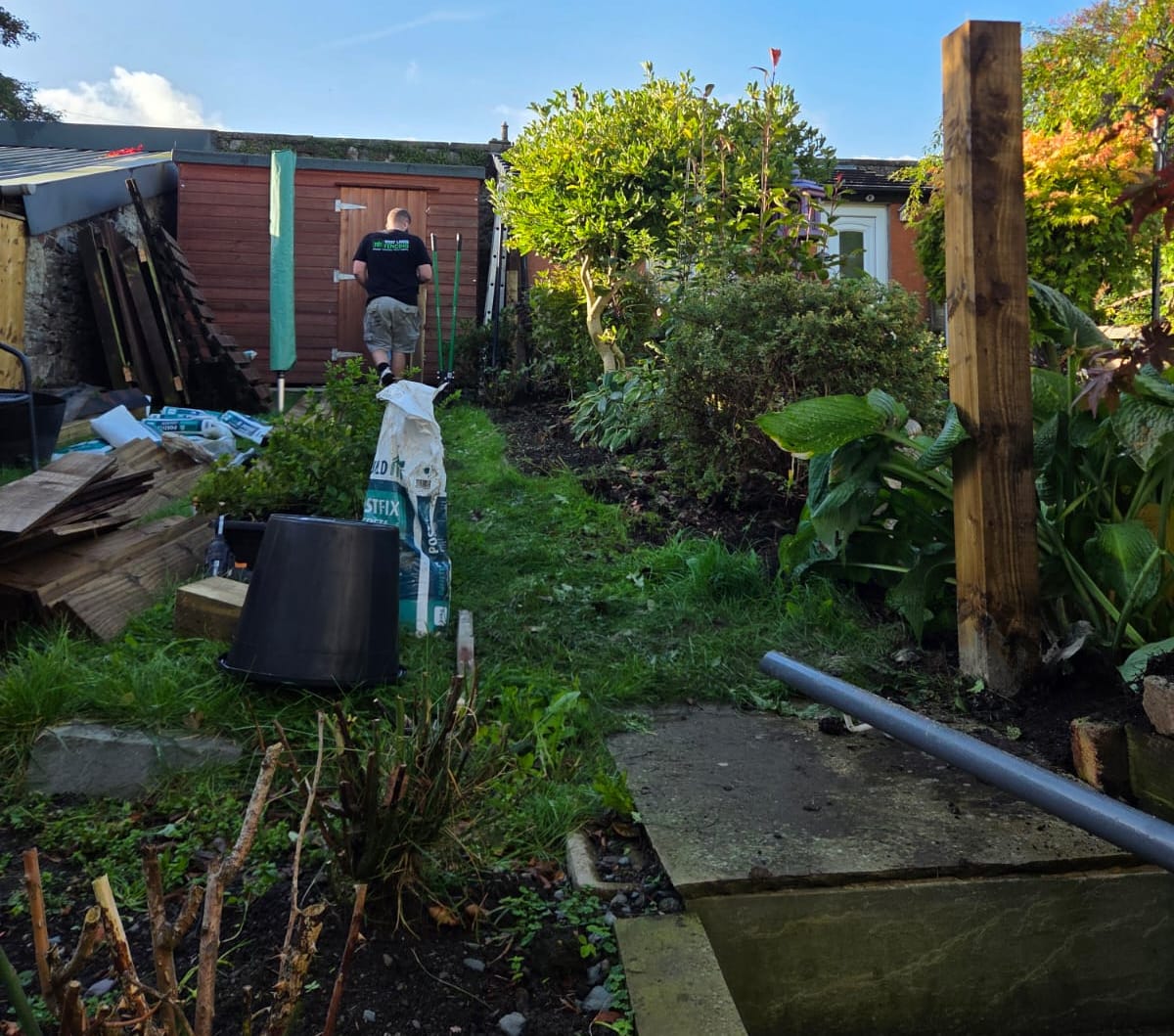 New timber fence post set beside a garden border with materials stacked on the lawn