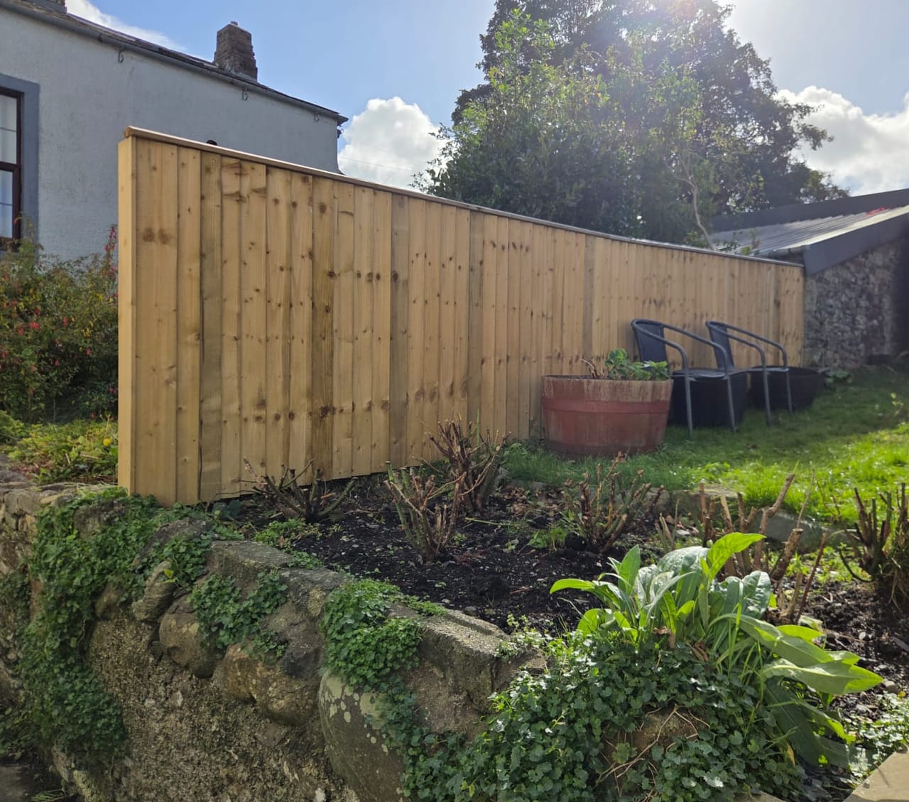 New featheredge fence with a capping rail behind a raised bed and stone wall